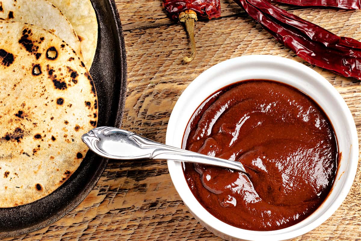 Naan bread in a cast-iron pan with a white bowl of red curry sauce and a silver spoon on a wooden table.
