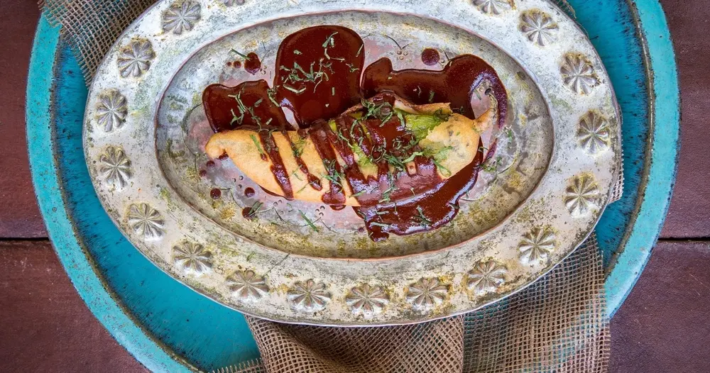 Plate with a plated entrée topped with dark sauce and green herbs on a decorative metal charger.