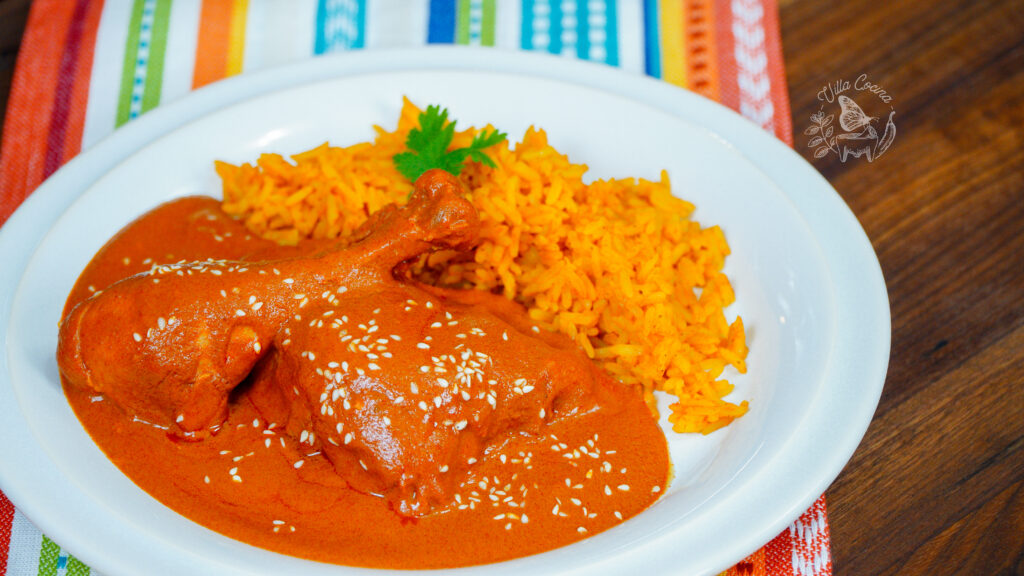Chicken leg in orange sauce with sesame seeds, served with yellow rice on a white plate.