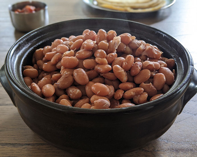 Roasted peanuts piled in a dark serving pot on a wooden table with a small dish in the background.