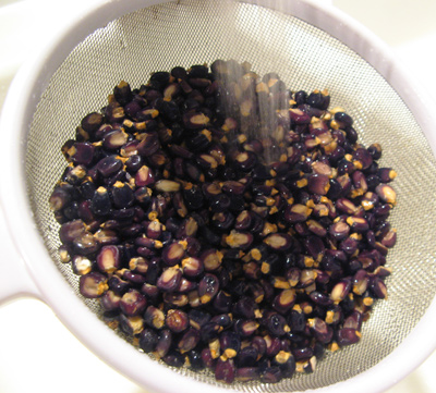 Colander with rinsed purple corn kernels soaking in water