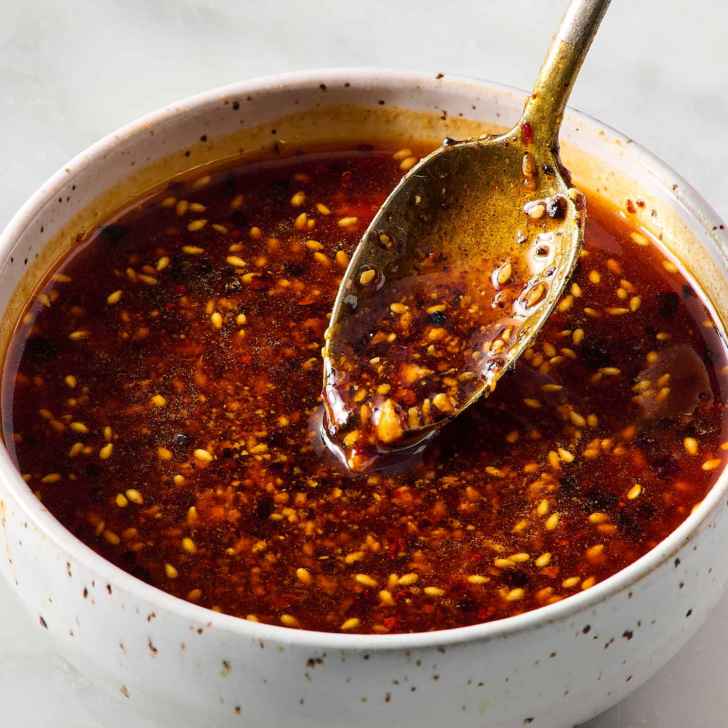Pot of spicy chili sauce with sesame seeds and a metal ladle resting in it.