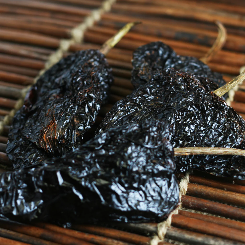 Close-up of glossy black prunes threaded on twine over a wooden striped rack, ready to dry